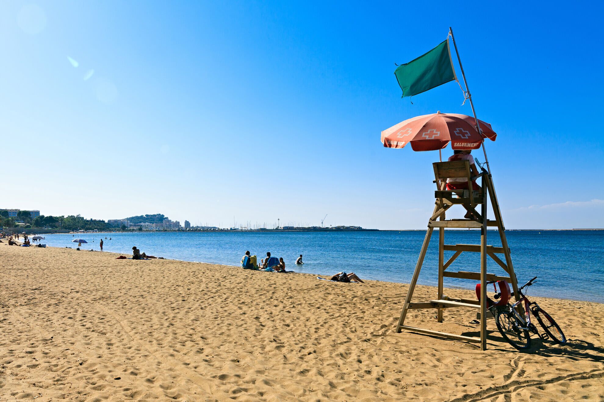 A lifeguard tower with a flag and an umbrella on a sandy beach.