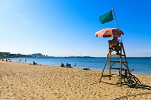 Una torre de salvavidas con una bandera y un paraguas en una playa arenosa.