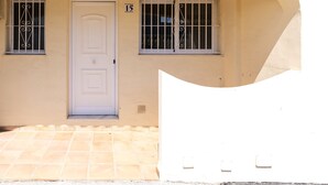 Un edificio con una porta bianca, due finestre con inferriate e il numero '15' sulla parete.