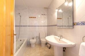 Une salle de bain avec une baignoire, deux toilettes, un lavabo et un miroir.
