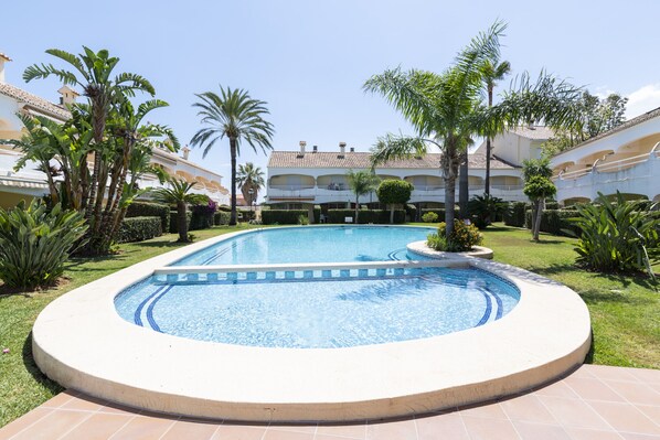 A pool surrounded by palm trees and a building with multiple balconies.