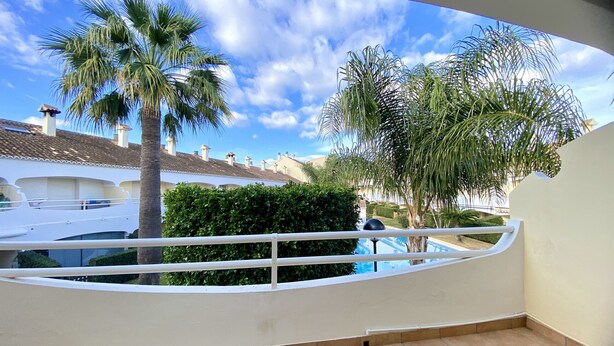 Een balkon met een witte railing met uitzicht op een woongebied met palmbomen en een helderblauwe lucht.