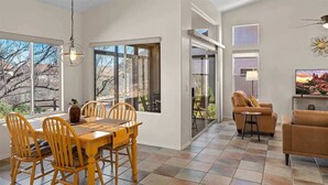 Comedor con mesa y sillas de madera, lámpara colgante y ventanas amplias con vistas a árboles y colinas.