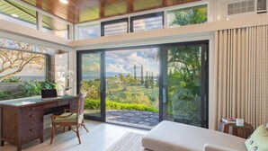 Quarto moderno com escrivaninha, cadeira e sofá, grandes portas de vidro com vista para o jardim.