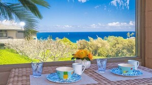 Uma mesa com duas chávenas, dois copos, um vaso de flores e vista para o oceano através de uma janela.