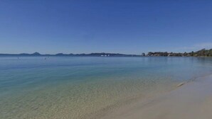 Una platja amb aigua cristal·lina, sorra daurada i muntanyes al lluny.