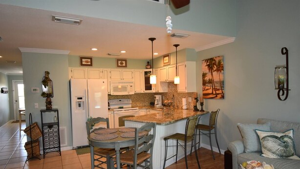 A kitchen with white cabinets, a central island, and a dining area with chairs. - 7G, Emerald Escape (Destin)