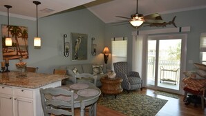 A spacious living area with a kitchen island, dining table, and chairs. There is a balcony with a view of palm trees. - 7G, Emerald Escape (Destin)
