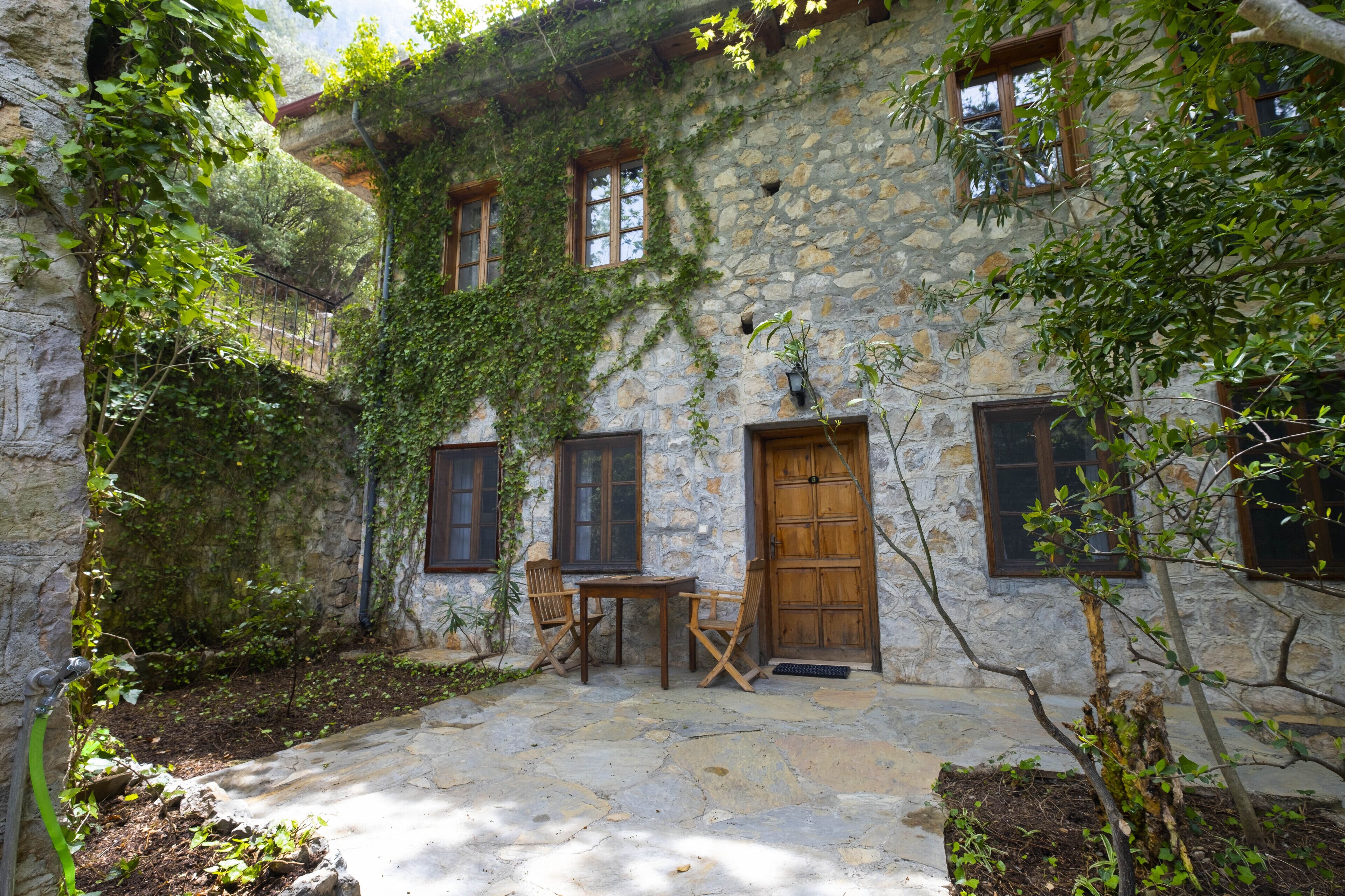 A stone building with ivy-covered walls, a wooden door, and a small outdoor seating area with a table and chairs.