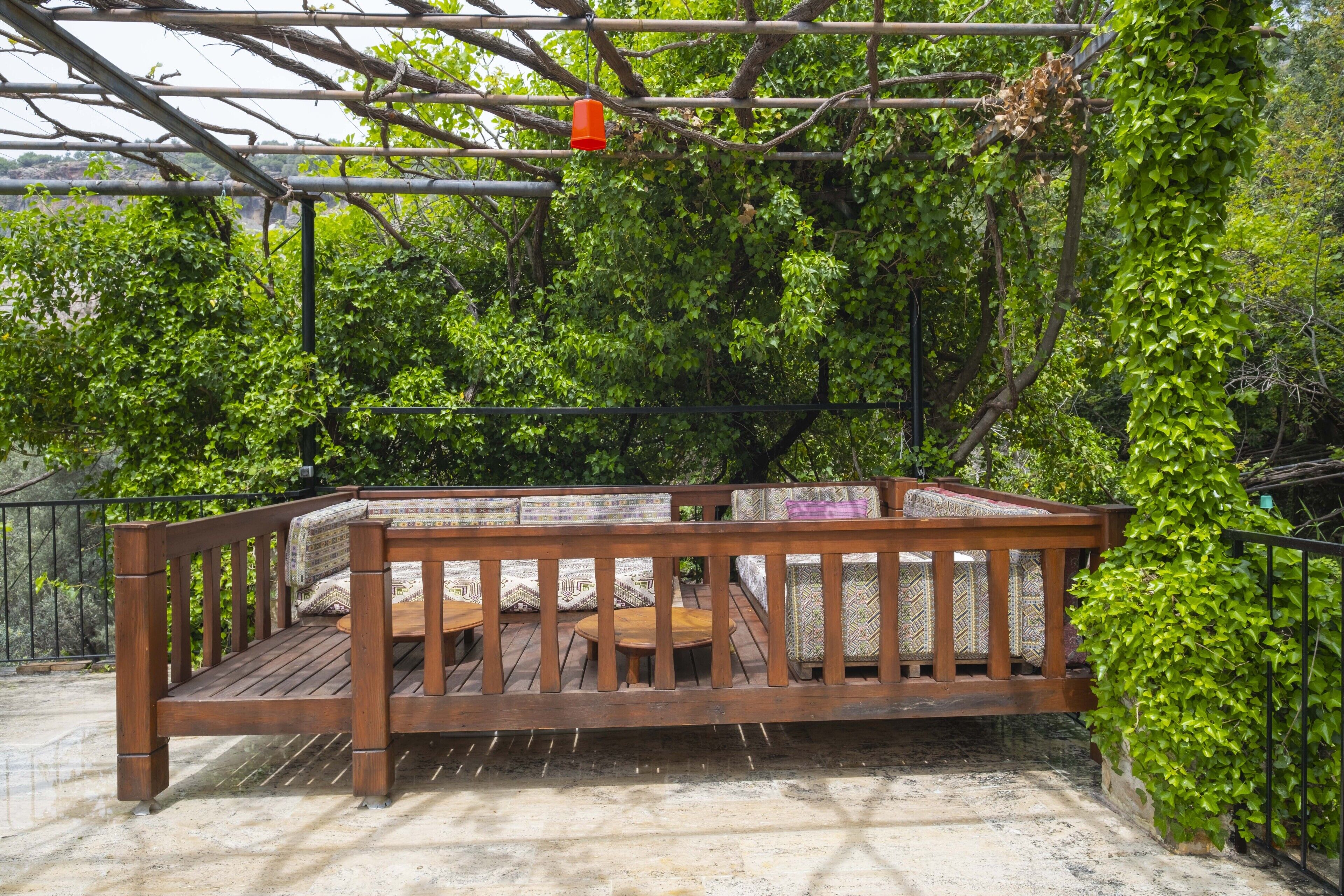 A wooden deck with a bench and tables, surrounded by lush greenery and a metal railing.