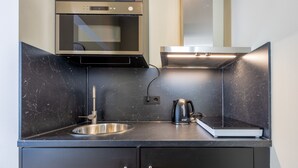 Une cuisine moderne équipée d’un four à micro-ondes encastré, d’un évier en acier inoxydable et d’une bouilloire posée sur le plan de travail.