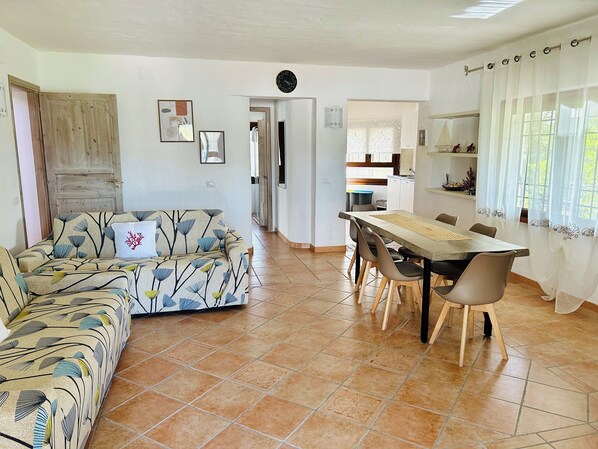 Een woonkamer met een bank, eettafel, stoelen en een keuken op de achtergrond.