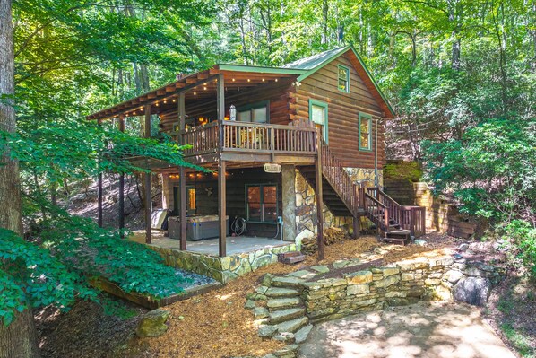 A cabin with a porch, a staircase, and a stone wall.