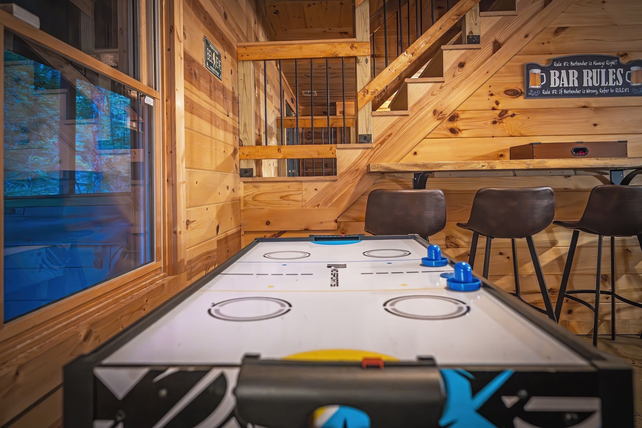 An indoor ice hockey table with a wooden interior, bar stools, and a sign with 'BAR RULES'.