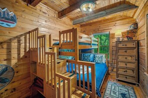 L’intérieur d’une cabane en bois, avec un lit superposé, une commode, un ventilateur et une fenêtre donnant sur les arbres.