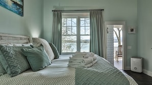 A bedroom with a large bed, a view through a window, and a door leading to a balcony. - A Lake Blue Ridge Cottage | Morganton, GA (Morgantown)