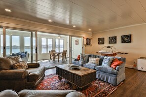 A spacious living room with a large sliding glass door leading to a balcony, a cozy seating area with a coffee table, and a dartboard on the wall.
