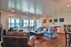 A spacious living room with a large sliding glass door leading to a balcony, a sofa set, a coffee table, and a dartboard on the wall.
