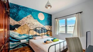 A bedroom with a bed, a window with a view, a wall mural, and a chair. - Villa Fedelian 1 with garden and heated pool (Playa Blanca)