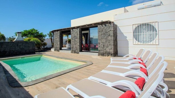 A pool area with lounge chairs and a stone wall. - Villa Fedelian 1 with garden and heated pool (Playa Blanca)