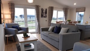 A modern living room with a grey sofa, a coffee table, and a dining area with a table and chairs. - Luxury 3 bedroom, pet-friendly lodge on the side of a beautiful fishing lake. (Clitheroe)