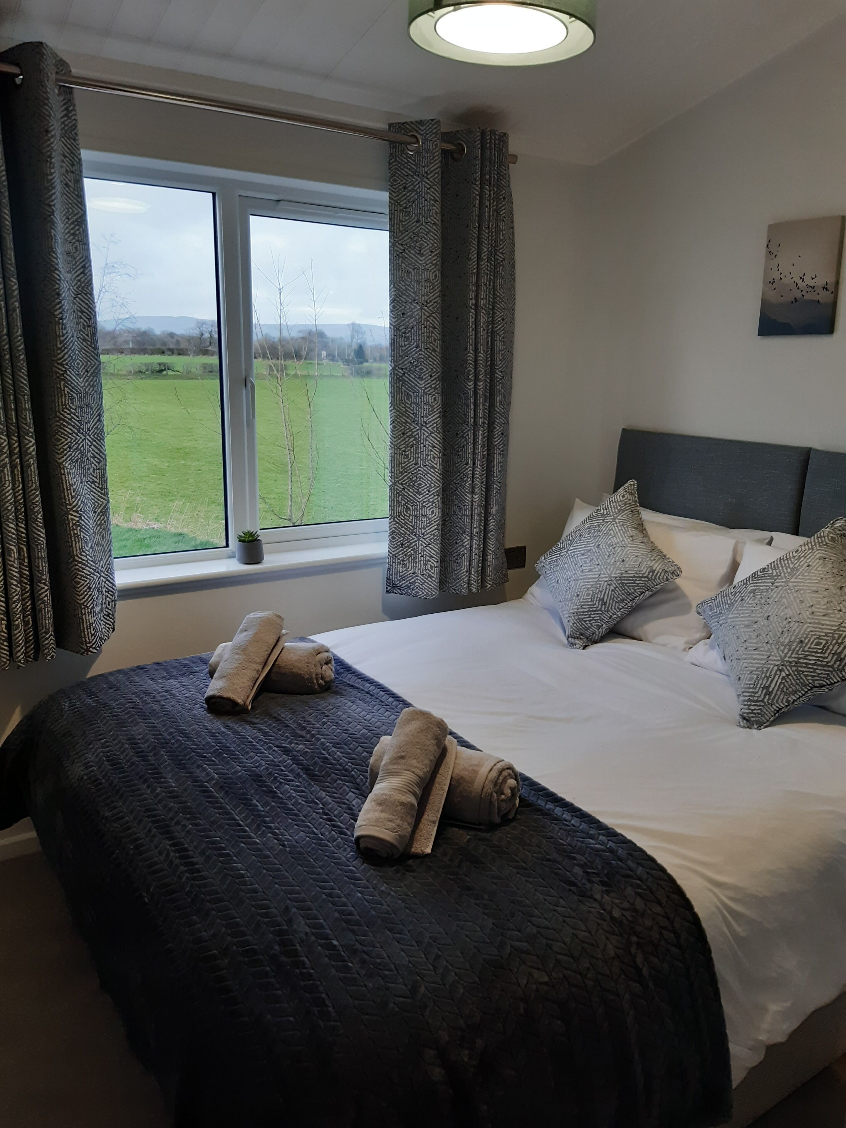 A bedroom with a large bed, patterned curtains, and a view of a green field.