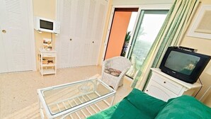 Una habitación con una cama, televisión, una silla, una mesita y un armario.