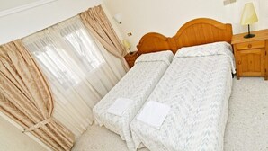 Un dormitorio con dos camas individuales, cabecero de madera, mesita de noche con lámpara y ventana con cortinas.