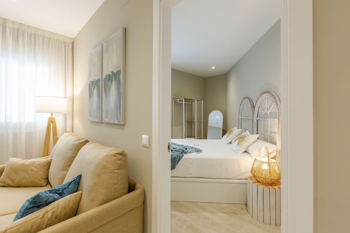 Una habitación de hotel moderna con sofá, cama con cabecera, mesita de noche con lámpara y espejo.