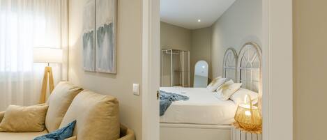 A modern hotel room with a sofa, a bed with a headboard, a bedside table with a lamp, and a mirror.