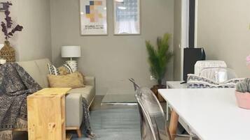 Ein gemütlicher Wohnbereich mit Sofa, Couchtisch, Esstisch mit Stühlen und zwei gerahmten Kunstwerken an der Wand.