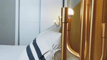 A bed with a white and blue striped pillow, a gold candelabra with a lit bulb, and a white door in the background.