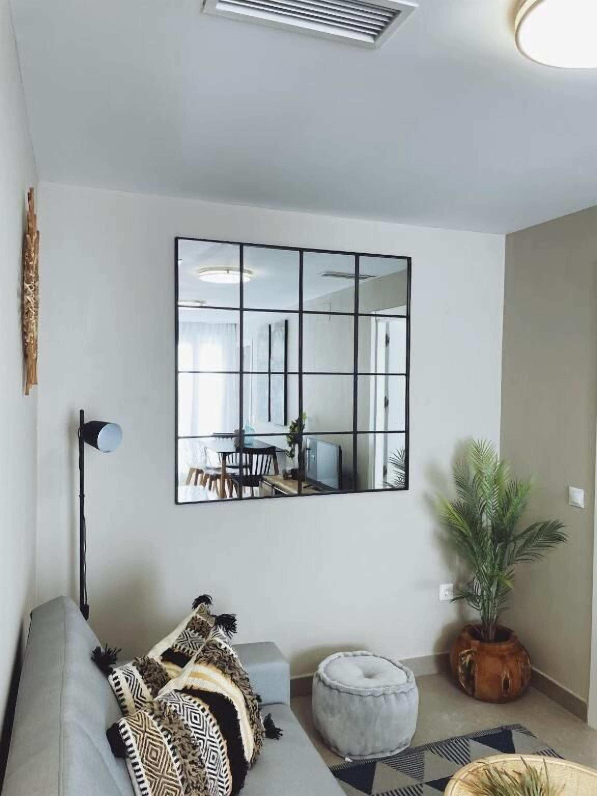 Una sala de estar moderna con un sofá modular, una lámpara de pie, un espejo grande, un comedor y una planta en maceta.