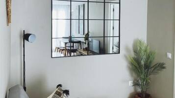 Una sala de estar moderna con un sofá modular, una lámpara de pie, un espejo grande, un comedor y una planta en maceta.