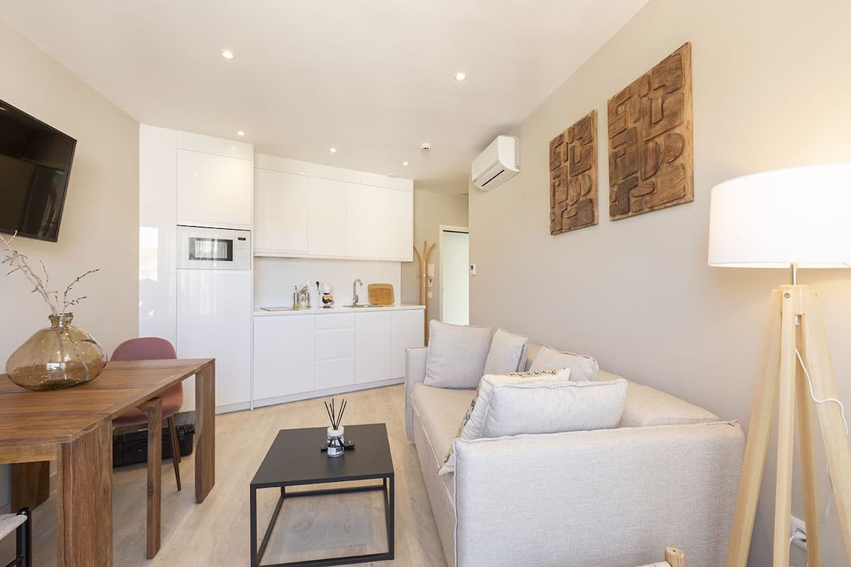 Un apartamento moderno con comedor, sofá, mesa de centro y cocina al fondo.