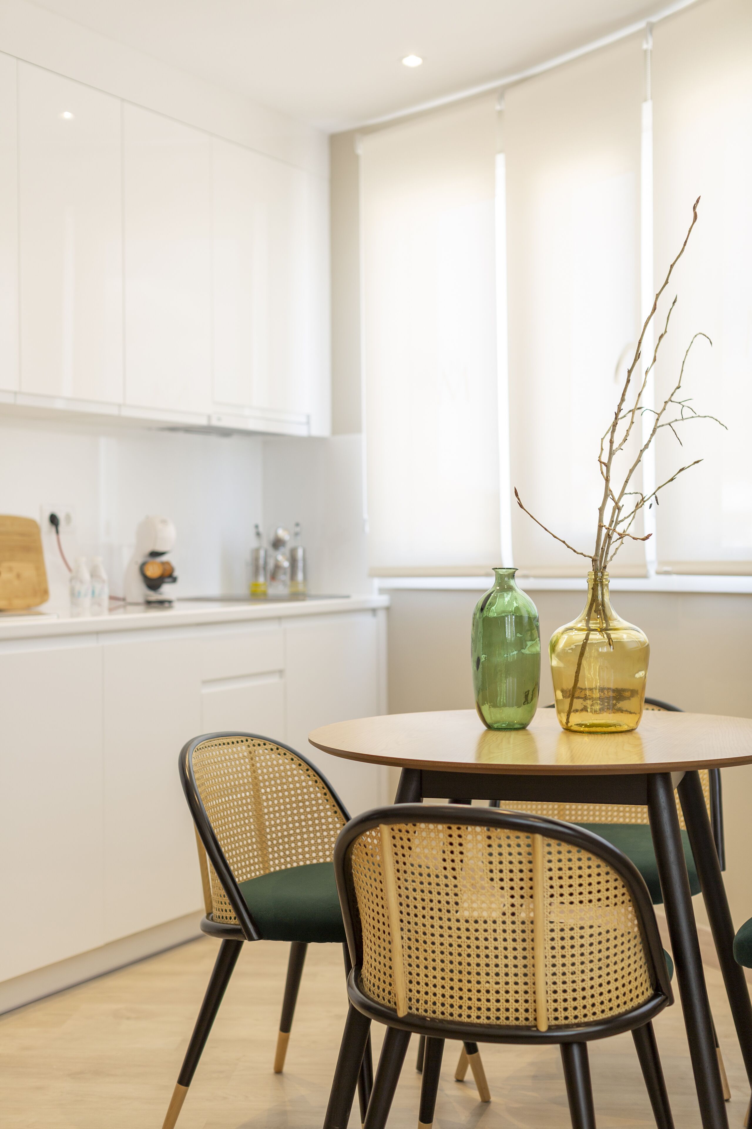Una cocina moderna con armarios blancos, una mesa redonda con dos sillas y un florero con ramas sobre la mesa.