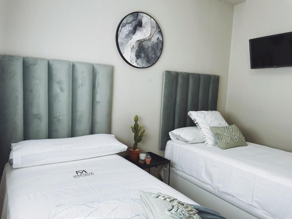A hotel room with two beds, a round wall art piece, a flat-screen TV, and a small table with a cactus.