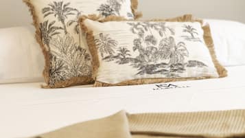 A bed with two decorative pillows featuring palm tree designs, a black tassel hanging from a fan, and a beige throw blanket.