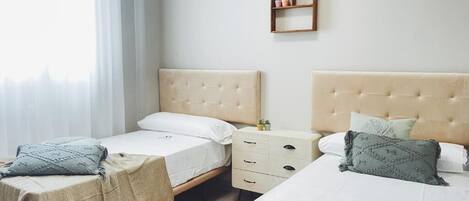 Un dormitorio con dos camas, una mesita de noche, un estante en la pared y una ventana con cortinas.