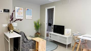 Una sala de estar moderna con televisor, muebles blancos, una mesita de madera y una planta.