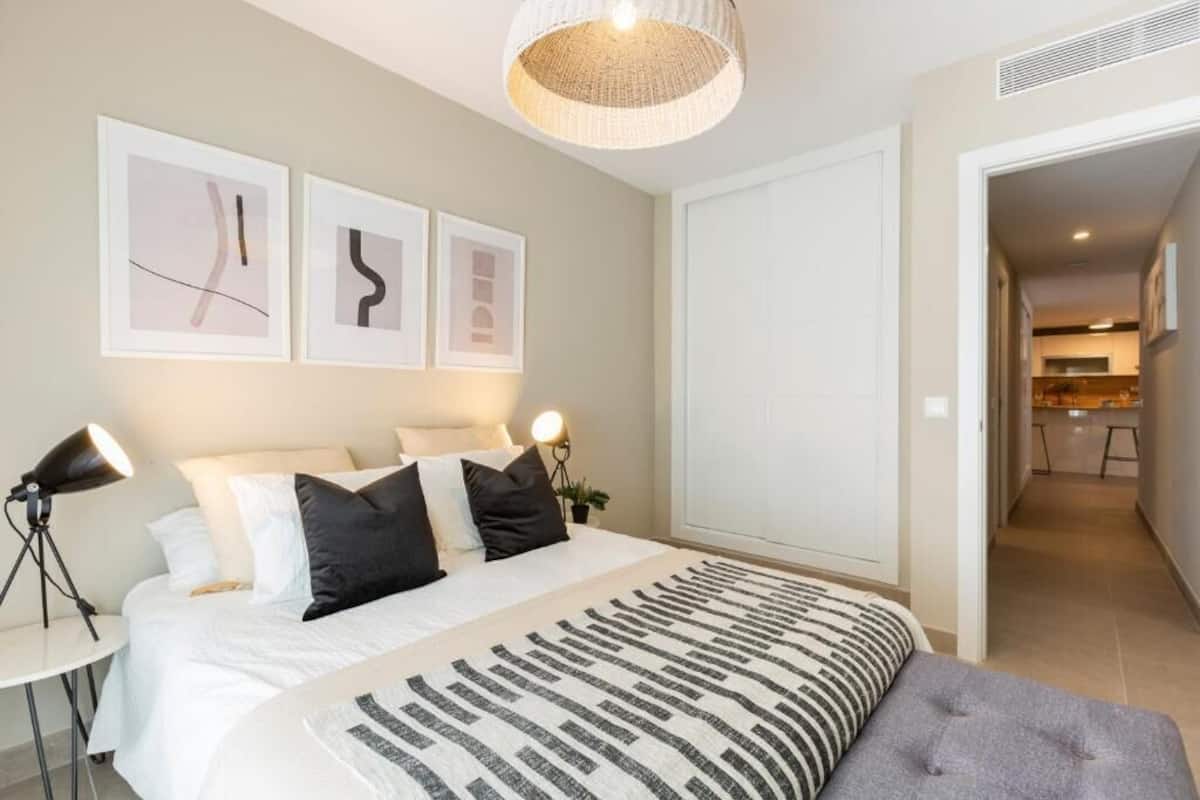 Un dormitorio con cama, mesitas de noche, una lámpara, un colgante de techo y cuadros en la pared.