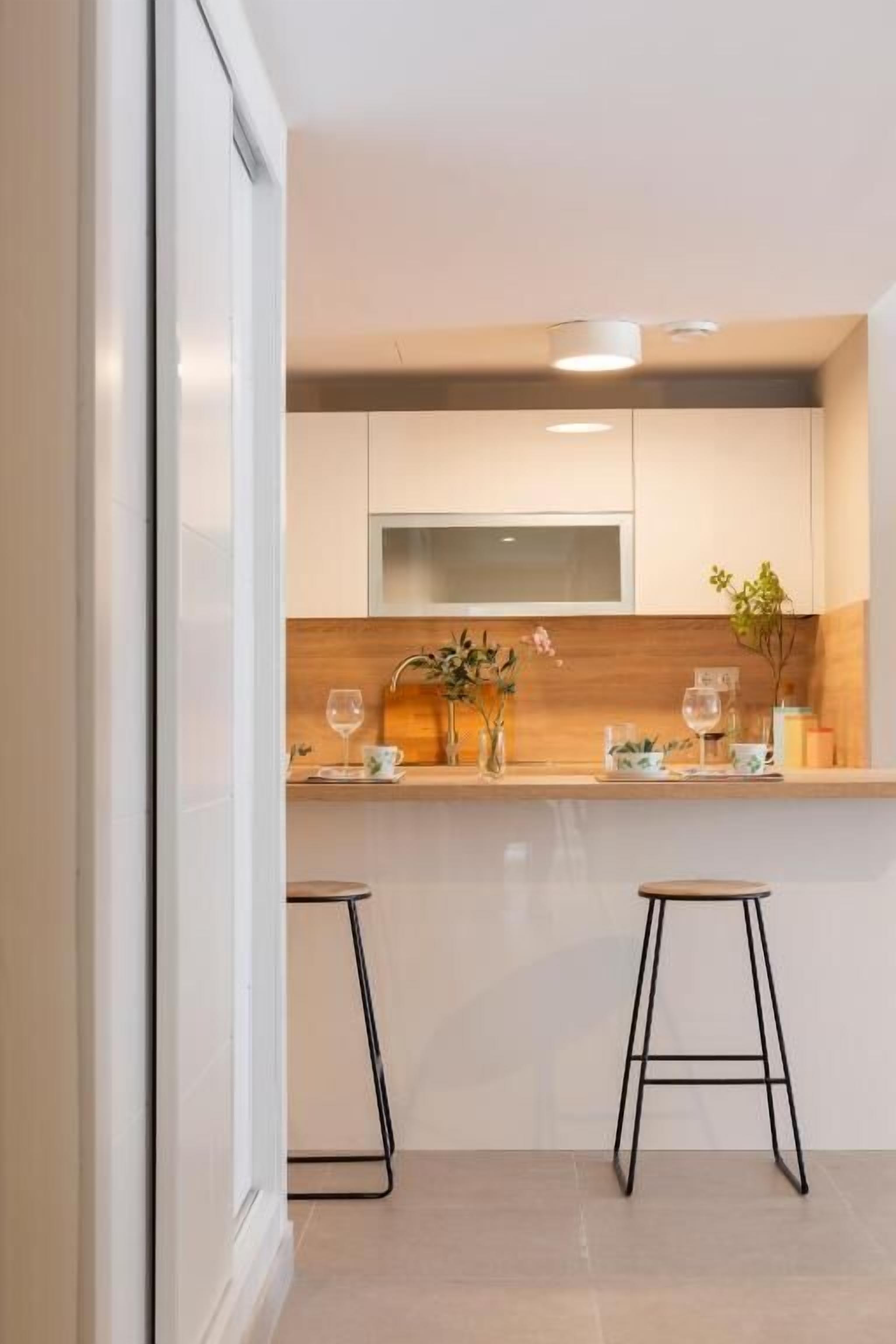 Una cocina moderna con encimera de madera, dos taburetes negros y un microondas.