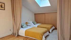 Un dormitorio con dos camas, suelo de madera, un tragaluz y un cuadro en la pared.