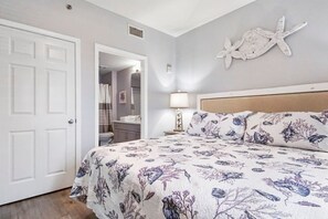 Une chambre à coucher avec un lit, une porte et une salle de bain visible à travers une porte ouverte, ainsi qu’un élément décoratif sur le mur.