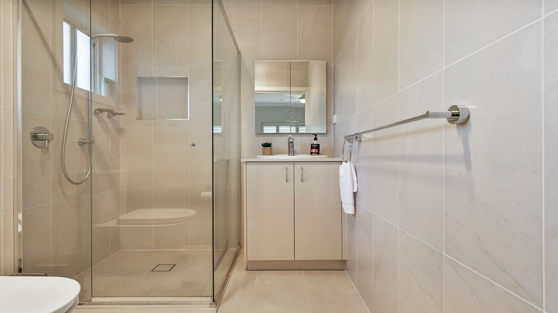 Un baño moderno con ducha envuelta en vidrio, inodoro, lavamanos con espejo y toallero.