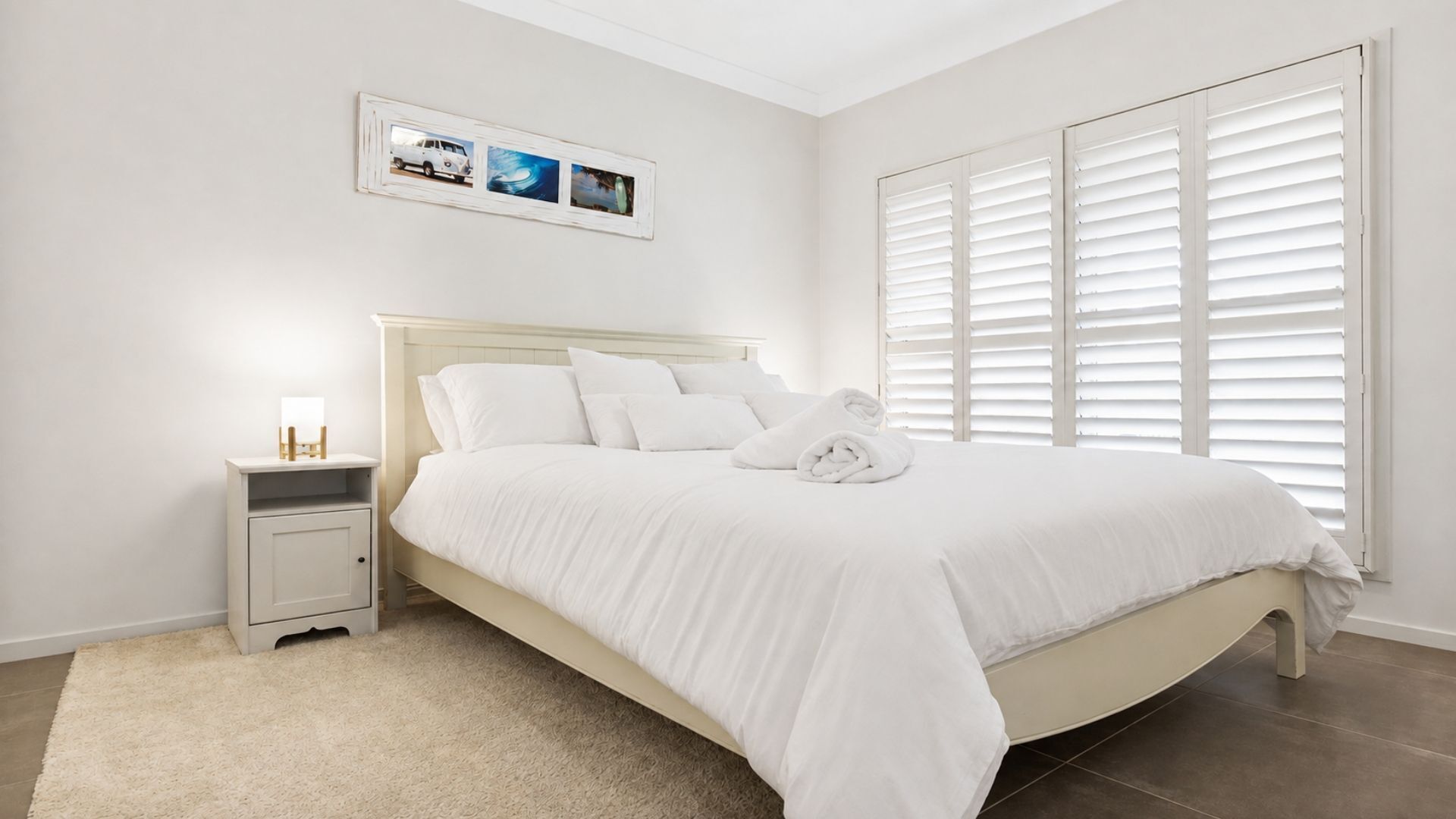Un dormitorio con cama, mesita de noche y ventana con persianas.