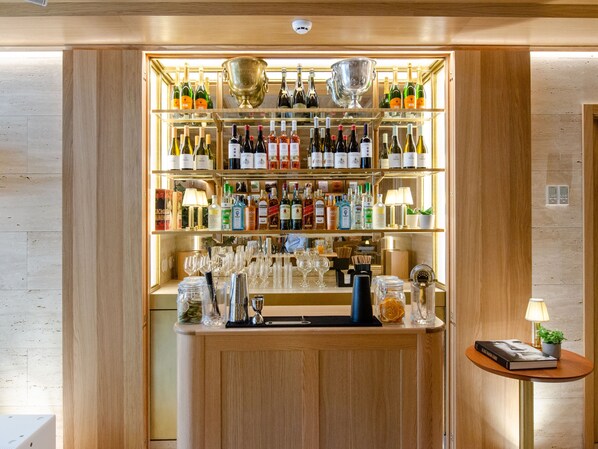 Zona de bar con estantes llenos de botellas de licores, vasos y una barra.