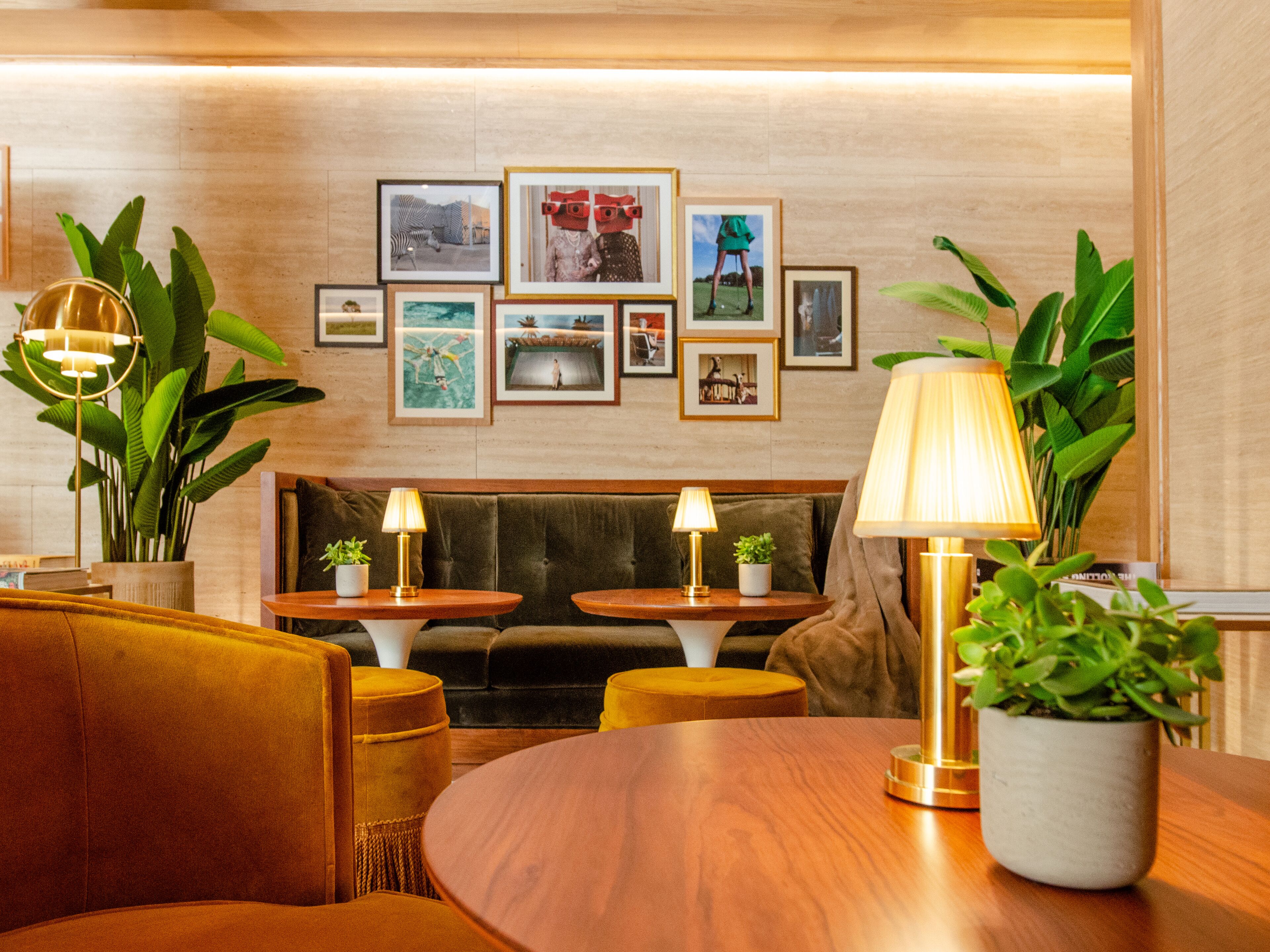 A modern hotel lobby with a wooden reception desk, two seating areas with lamps, and a wall decorated with framed pictures.