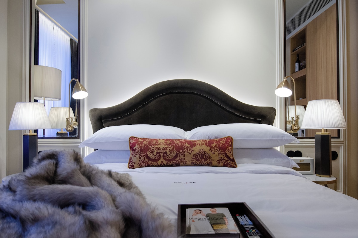 A hotel room with a large bed, two bedside lamps, a nightstand, a remote control, and a book.