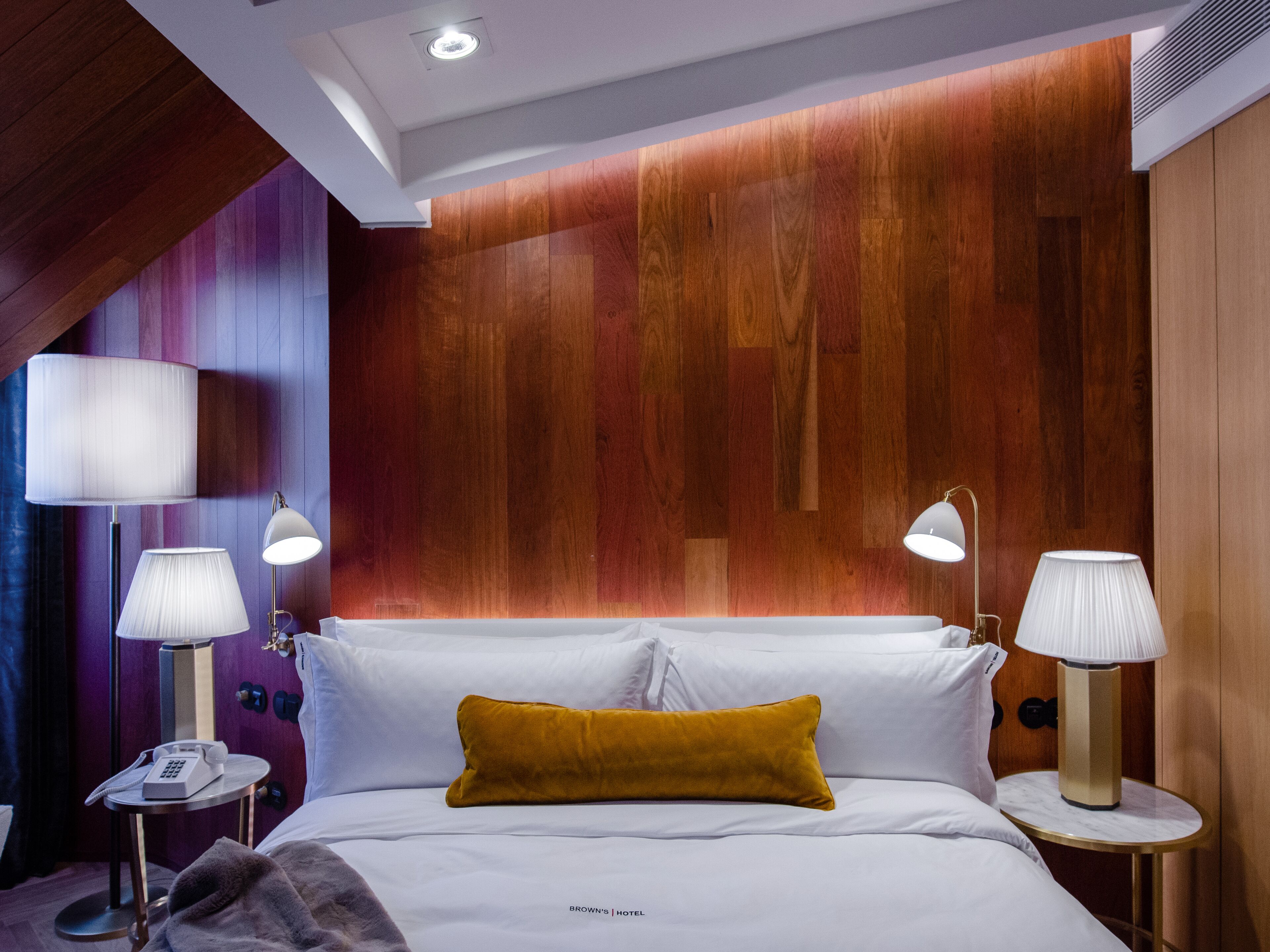 Una habitación de hotel con cama, dos mesitas de noche con lámparas, teléfono y una pared decorativa de madera.